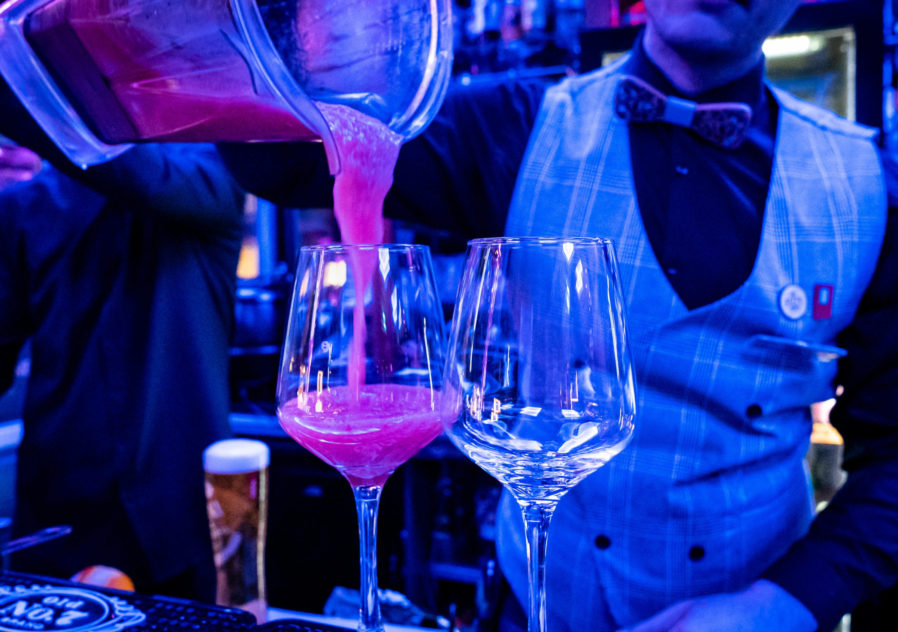 Bartender pours strawberry daiquiri from a mixer into a cocktai glass